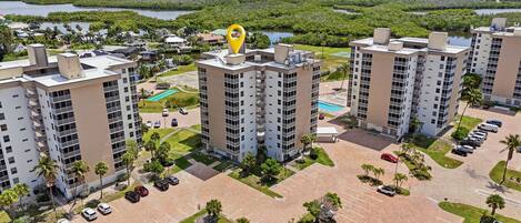 A high-rise residential building complex with multiple parking lots, a swimming pool, and surrounding greenery.