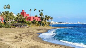 A beach with a red building, palm trees, and a clear blue sea. - Front line beach Benalmádena La Perla Playa Paraíso (BENALMÁDENA)