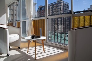 Une chambre moderne avec une grande fenêtre, une chaise blanche, une petite table avec un ordinateur portable et une tasse de café.