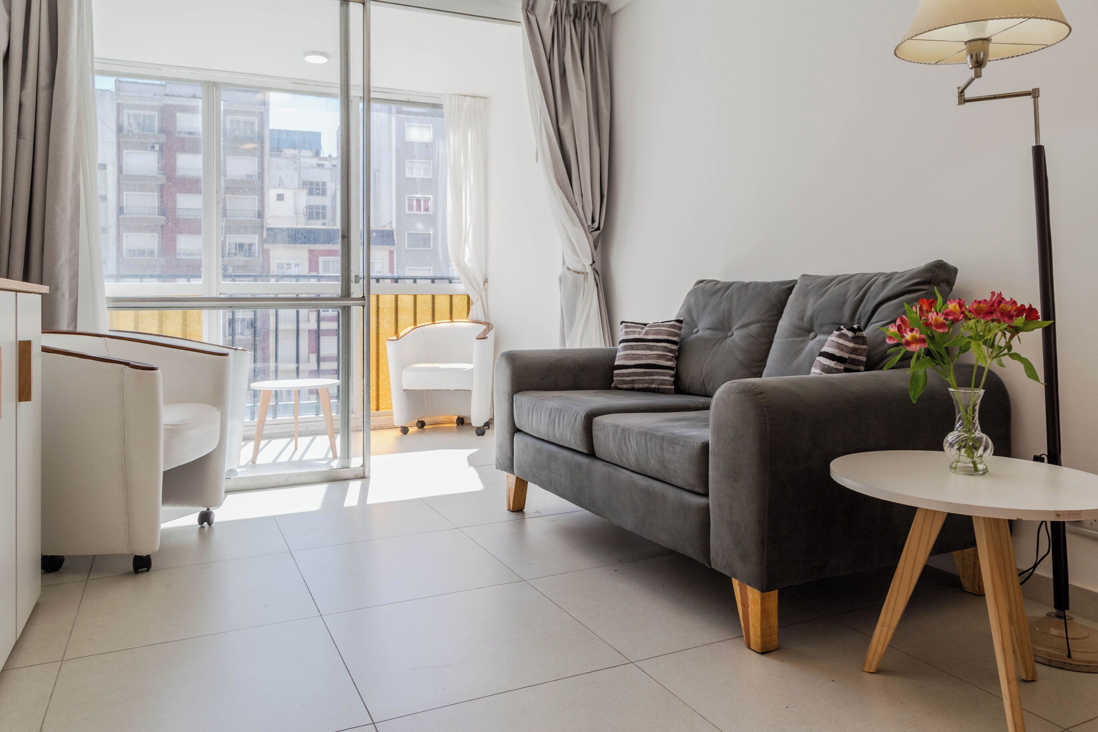 Een moderne woonkamer met een grijze bank, een kleine ronde tafel met een bloevas, een witte fauteuil en een vloerlamp.
