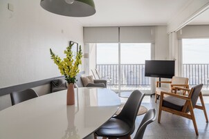 Una sala de estar moderna con una gran mesa blanca, asientos cómodos, un televisor de pantalla plana y un balcón con vistas.