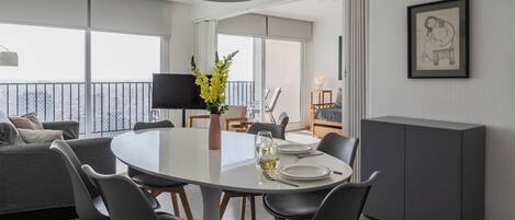 A modern dining area with a round table, black chairs, a vase with flowers, and a television in the background.