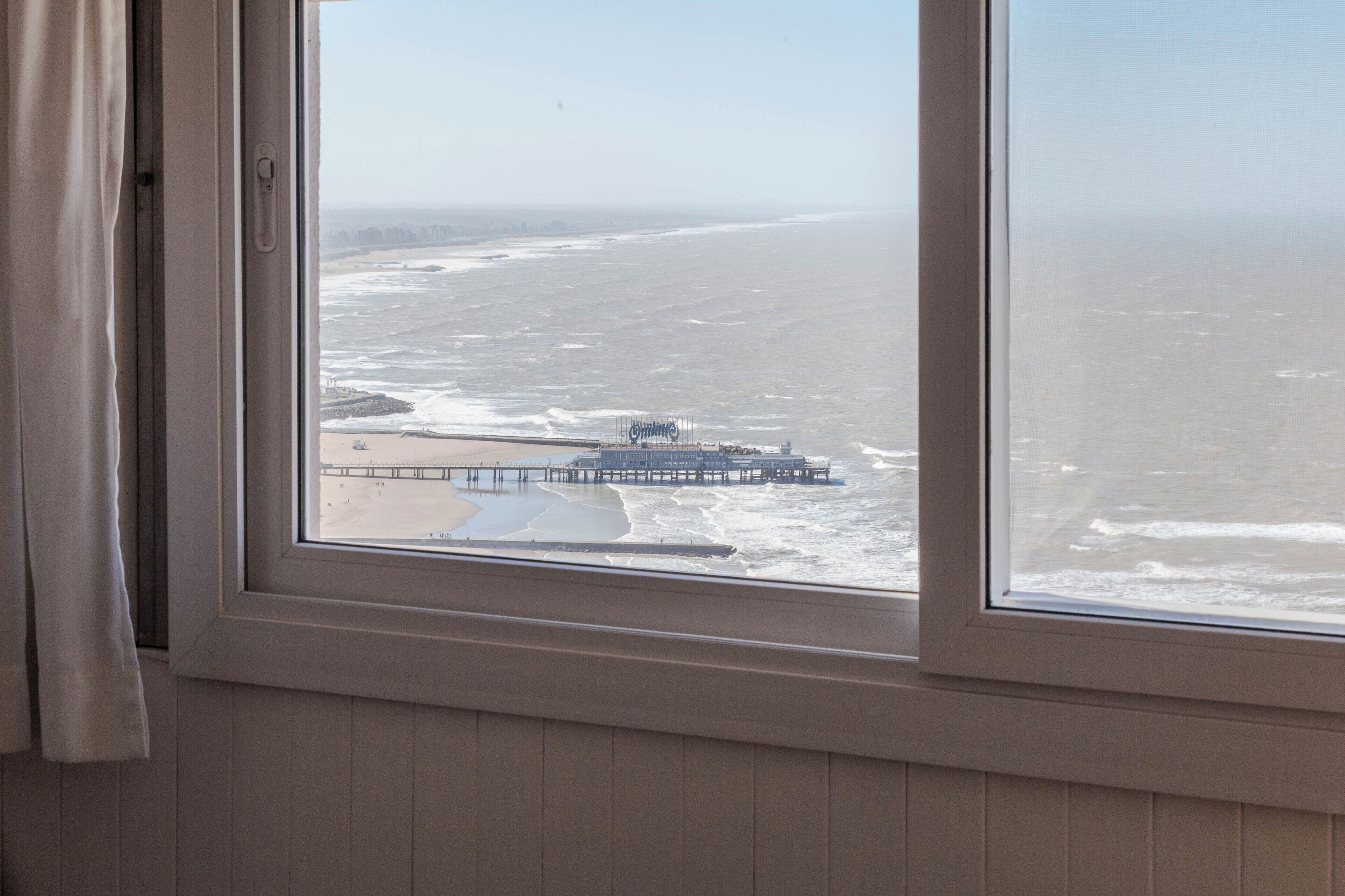 A view from a room with a window overlooking a beach and a pier.