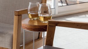 A wooden chair with a cushioned seat and backrest, a small wooden table with two glasses of white wine, and a glass door leading to an outdoor area with a metal railing. - BT Homes - Mar del Plata, Av. Colon (Mar del Plata)