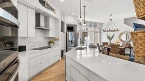 A modern kitchen with white cabinetry, a stainless steel refrigerator, and a large island with a sink. - Charming Beach Cottage, 2 Pools and Tennis Access + Free Attraction Tickets! (Santa Rosa Beach)