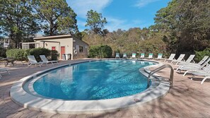 En swimmingpool med solstolar och en byggnad i bakgrunden.