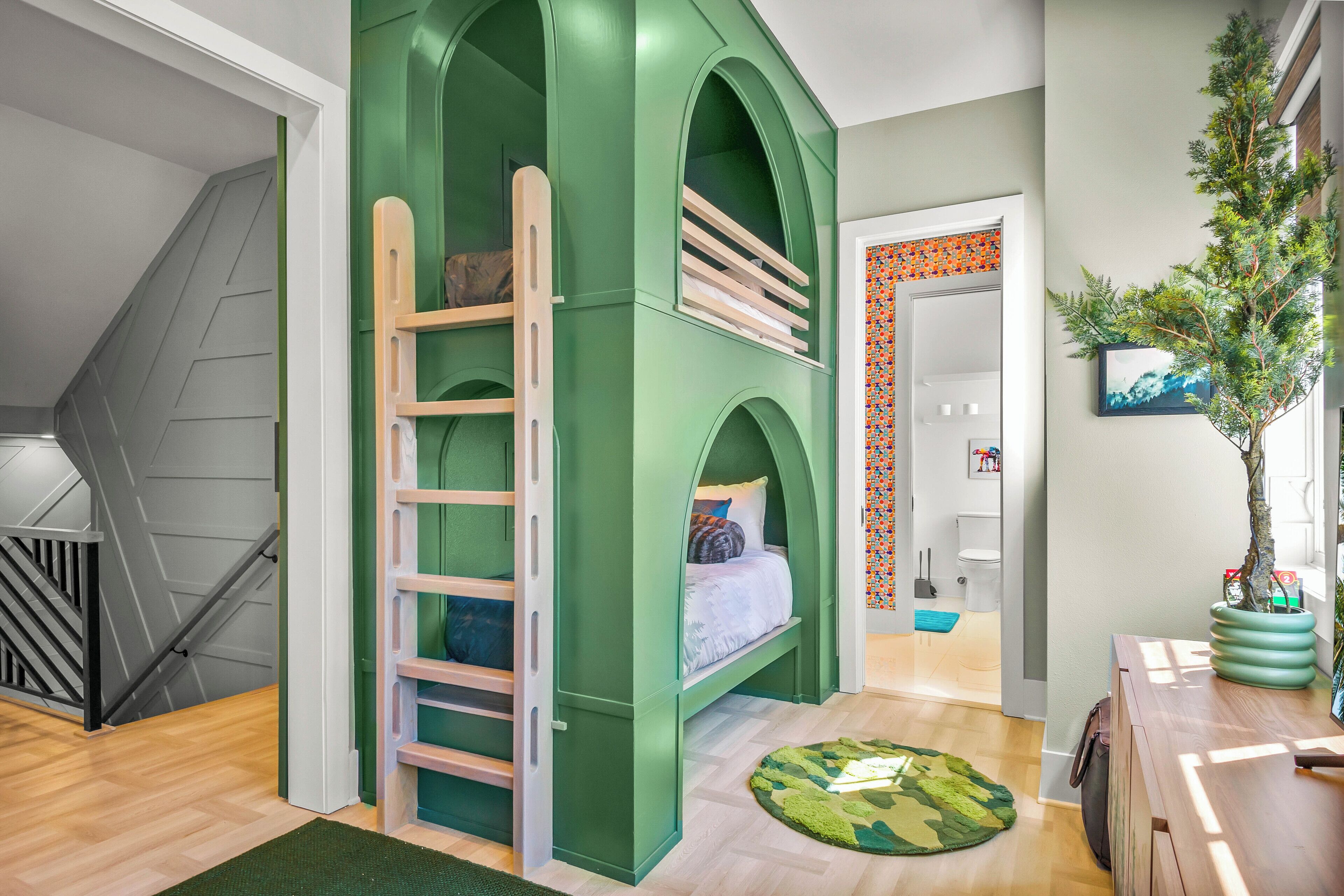A room with a bunk bed, a ladder, a small rug, a staircase, and a potted plant.