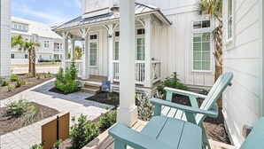 A white building with a covered porch, a small garden, and a blue chair. - Stella Maris 160 Tai-e (Port Aransas)