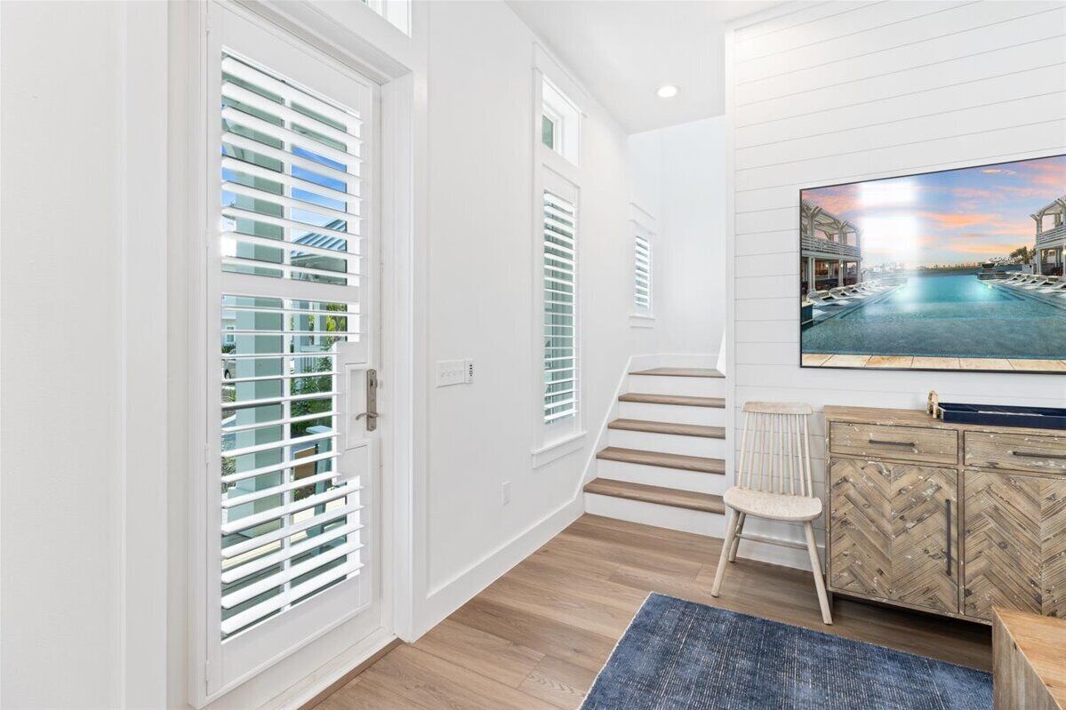 A modern interior with white walls, a wooden floor, a staircase, a herringbone-patterned cabinet, and a framed picture of a pool.