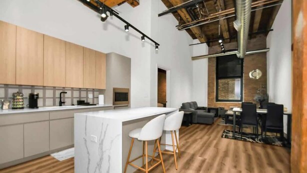 A modern kitchen with a marble island, wooden cabinets, and a dining area with a table and chairs. - River North Rooftop With In and Out Parking 3 (Chicago)