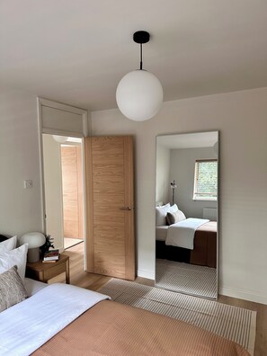 Un dormitori amb llit, taula de nit, làmpada i un mirall que reflecteix l'habitació.