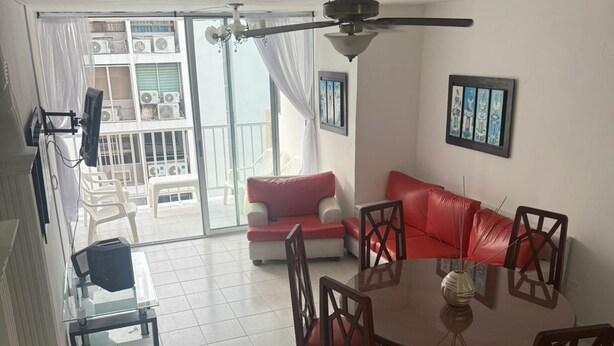 A dining area with a round table and chairs, a red sofa, and a ceiling fan. - Private apartment 🍃 with sea view 🥳🌇🌊 edf el morro (Santa Marta)
