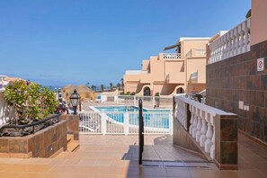 Zona de piscina en la azotea con vista al mar, rodeada de edificios con balcones y un cartel de prohibido fumar.