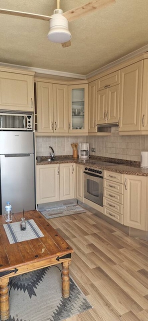 A kitchen with wooden cabinets, a stainless steel refrigerator, a coffee maker, and a wooden dining table.