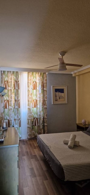 A bedroom with a bed, a ceiling fan, a framed picture on the wall, and a window with curtains. - Condo in Costa Adeje · ★4.75 · 1 bedroom · 1 bed · 1 bath (Costa Adeje)