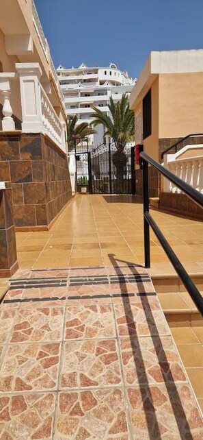 A corridor with tiled flooring leading to a gated entrance, a staircase, and a view of a multi-story building with balconies. - Condo in Costa Adeje · ★4.75 · 1 bedroom · 1 bed · 1 bath (Costa Adeje)