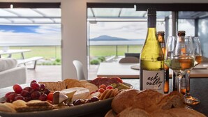 A table with a bottle of wine, glasses, and a charcuterie board with various cheeses, fruits, and bread. - Absolute Lakefront | Panoramic Views & Spacious Stay for 10 (Rotorua)