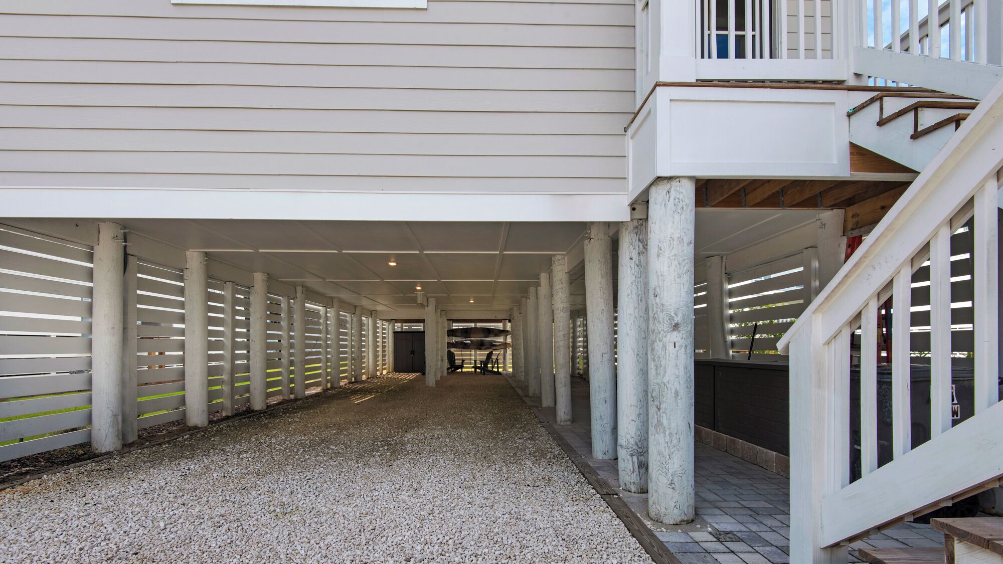 A covered walkway with a gravel floor, white railings, and a staircase leading to a balcony.