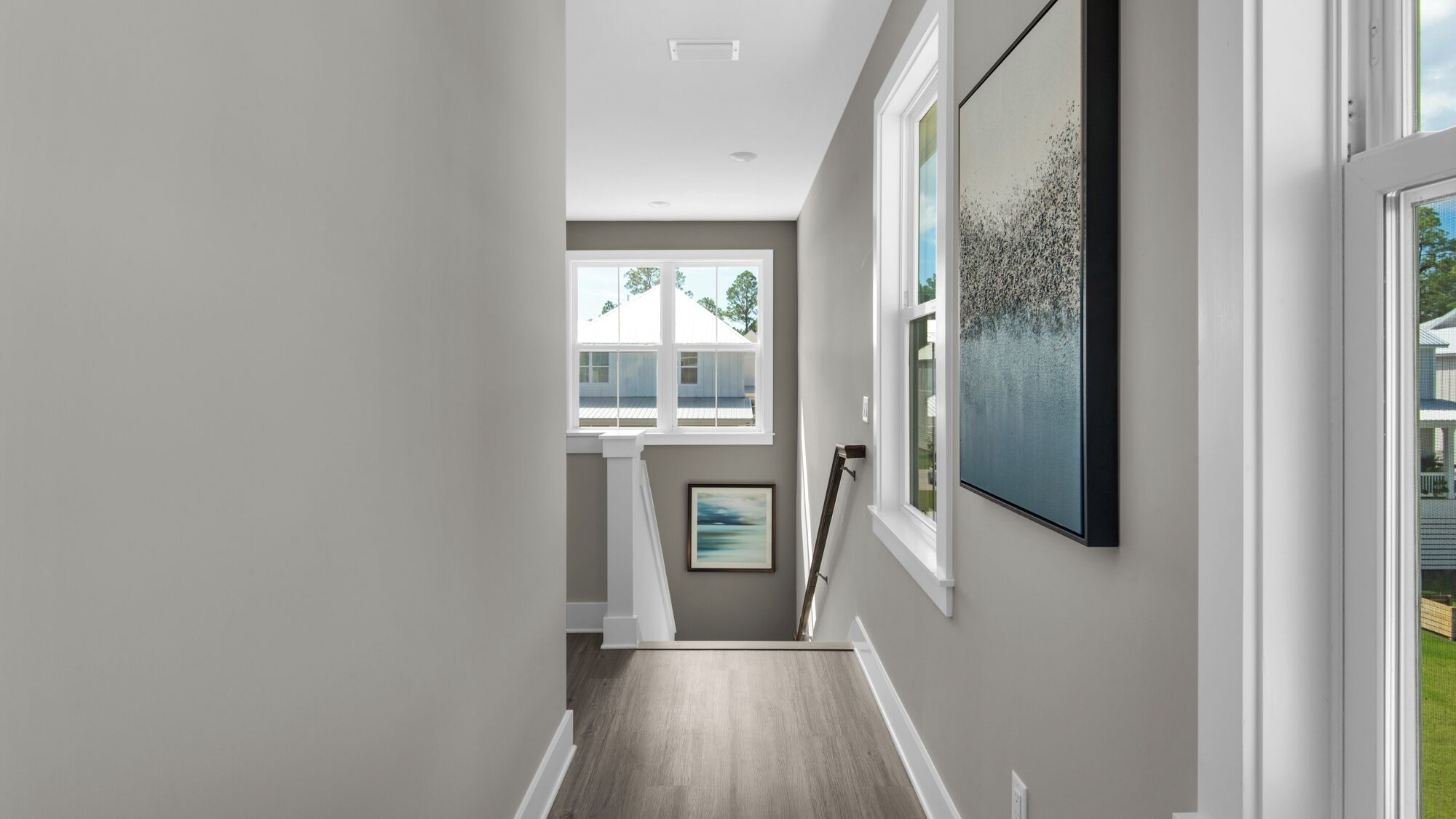 A hallway with a staircase leading to a second floor, a large window with a view of the outside, and a framed artwork on the wall.