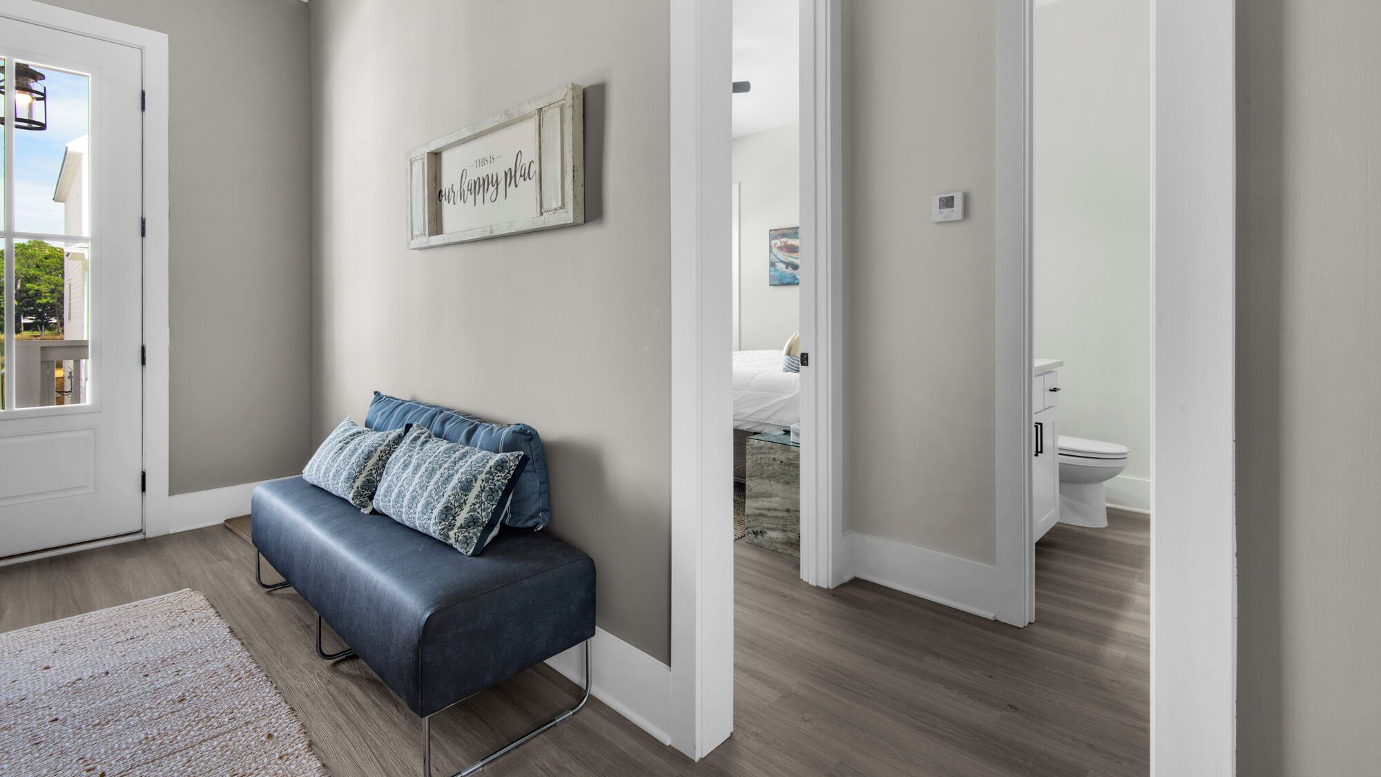 Ein modernes Interieur mit einer Sitzbank, einem gerahmten Schild und Blick in ein Badezimmer.