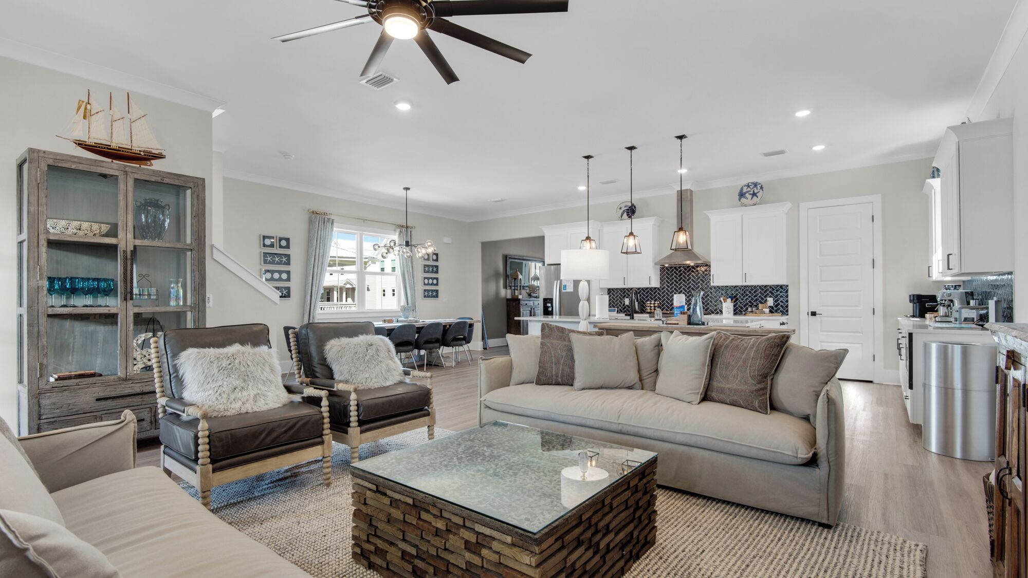 A spacious living room with a sofa, chairs, a coffee table, and a dining area. There is a kitchen in the background with modern appliances.