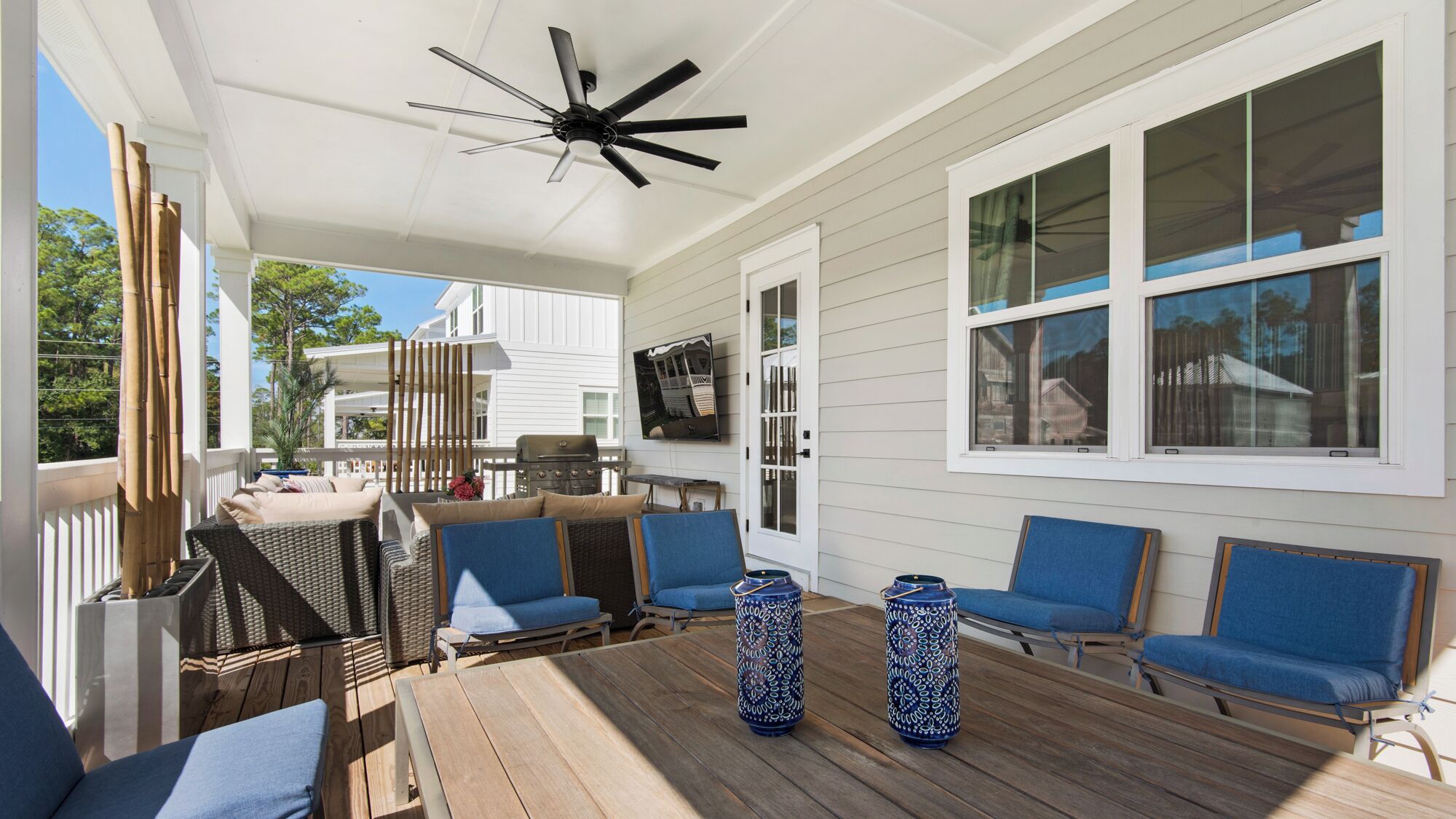 Een overdekt terras met een houten tafel, blauwe stoelen en twee decoratieve vazen.