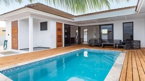 Ein modernes Haus mit Swimmingpool, Holzterrasse und Gartenmöbeln.