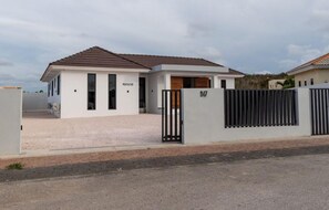 Une maison moderne à deux étages, dotée d’une allée fermée par un portail et d’une cour avant recouverte de gravier.