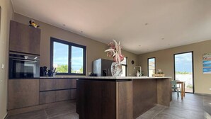 Una cocina moderna con armarios oscuros, una isla central y amplias ventanas que dejan entrar luz natural.