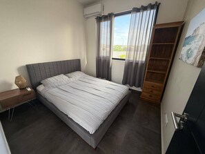 Un dormitorio con cama, mesita de noche, lámpara, armario y ventana con cortinas.