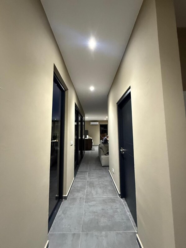 A corridor with doors on both sides, leading to a seating area with tables and chairs.