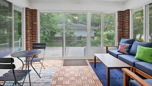 Une véranda avec une porte-fenêtre coulissante, un ventilateur de plafond, un canapé avec des coussins, une table et des chaises.