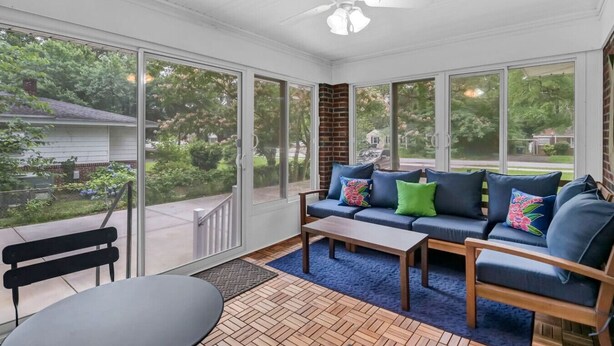 Une véranda avec une grande porte-fenêtre coulissante, un ventilateur de plafond, un canapé bleu agrémenté de coussins colorés et une table basse en bois.