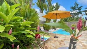 Un espace aménagé au bord de la piscine, avec une terrasse en pierre, une table ronde et un fauteuil de relaxation.