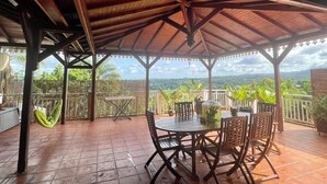 Une terrasse couverte avec une table et des chaises, un hamac et une vue sur le paysage.