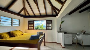 Une chambre à coucher avec un lit, un bureau et une chaise. Il y a une fenêtre qui donne sur un paysage verdoyant et un ciel nuageux.