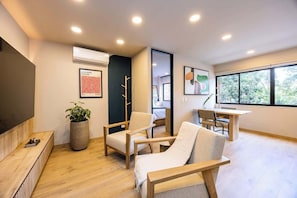 A modern living room with a flat-screen TV, a large potted plant, and a dining area with a table and chairs.