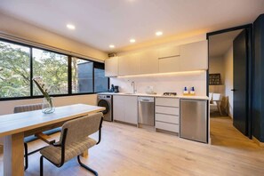 A modern kitchen with a dining area, large windows, and a view of trees. - Digital Nomad Paradise ~1BR unit in Manila’s Heart (Medellín)