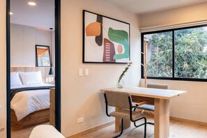 A modern hotel room with a bed, a desk with a chair, a large window, and a framed abstract painting on the wall. - Digital Nomad Paradise ~1BR unit in Manila’s Heart (Medellín)