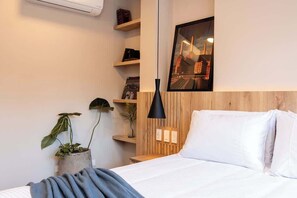 Ein modernes Schlafzimmer mit einem Holzkopfteil, einem Bett mit weißen Leinen, einer schwarzen Pendelleuchte und einem Stadtbild.