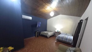 Een kamer met betegelde vloer, een bank, twee bedden, een kleine tafel en een airconditioner.