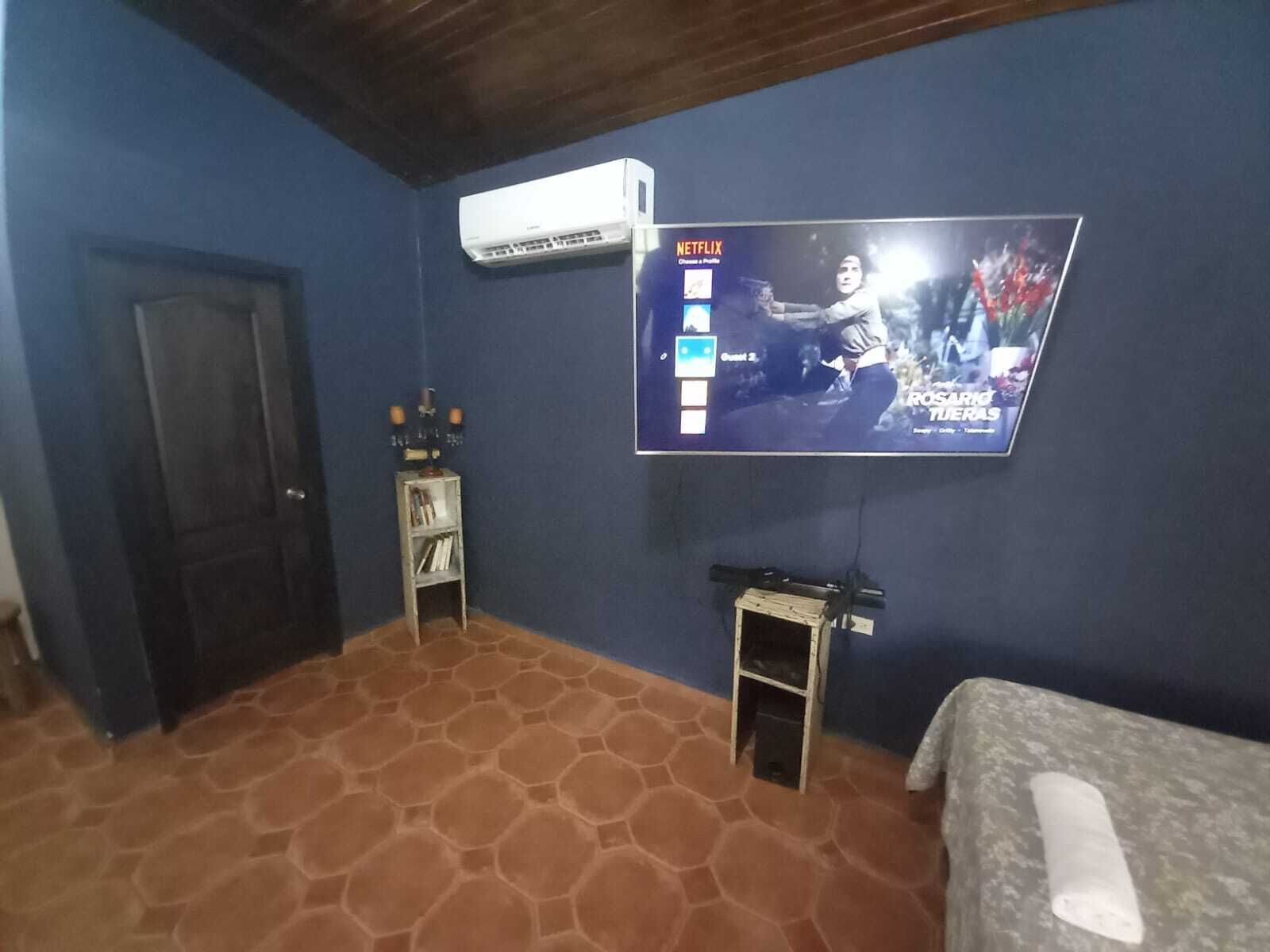 A hotel room with a television mounted on the wall, a small table with a lamp, and a bed with a blanket.