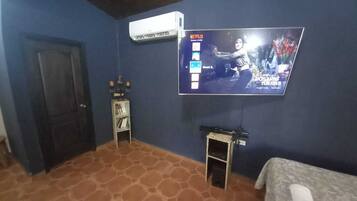 A hotel room with a television mounted on the wall, a small table with a lamp, and a bed with a blanket.