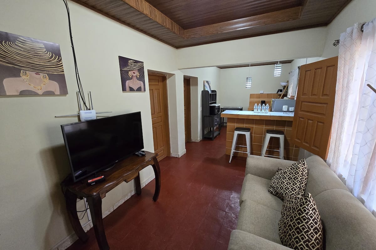 Ein Wohnzimmer mit Fernseher, einer Couch und einer Küche im Hintergrund.
