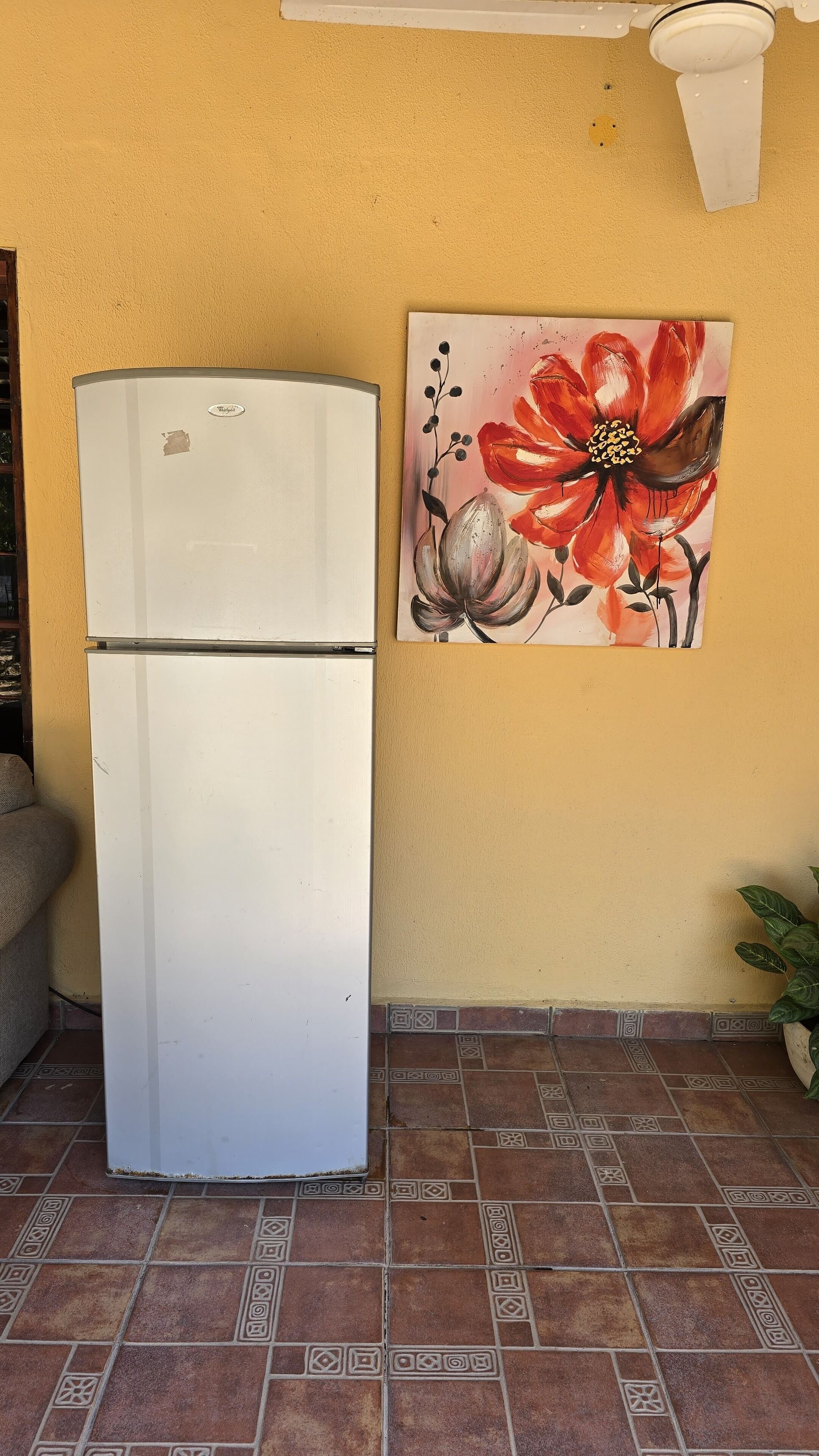 A white refrigerator against a yellow wall with a floral painting.