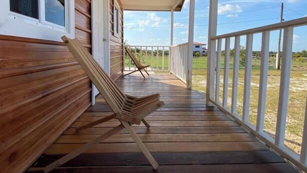 Une véranda en bois avec une balustrade blanche, une chaise pliante et une vue sur un champ verdoyant.