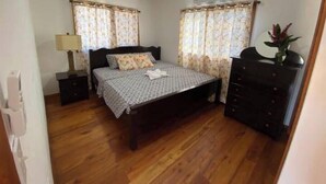 Une chambre à coucher avec un lit, une commode, une lampe et des rideaux.