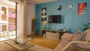 Sala de estar com mesa de centro de vidro, sofá, TV fixada na parede e varanda com vista.