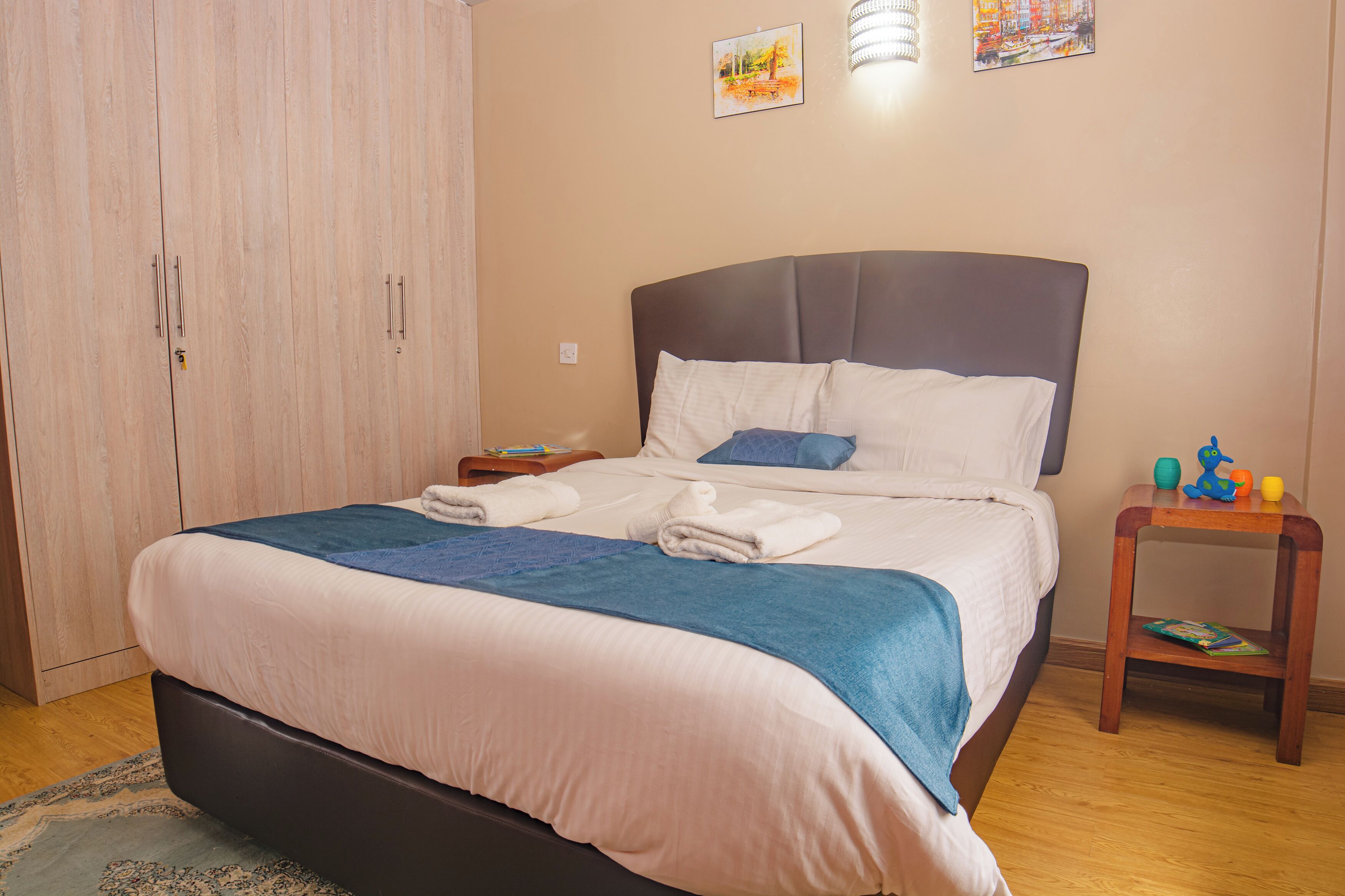 A neatly made bed with a blue and white duvet, a wooden nightstand with a lamp, and a wooden wardrobe.