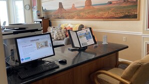A hotel reception desk with a computer, a framed painting of a desert landscape, and a sign indicating 'EMPLOYEES ONLY'. - Highland Estates Condotel (Mesquite)
